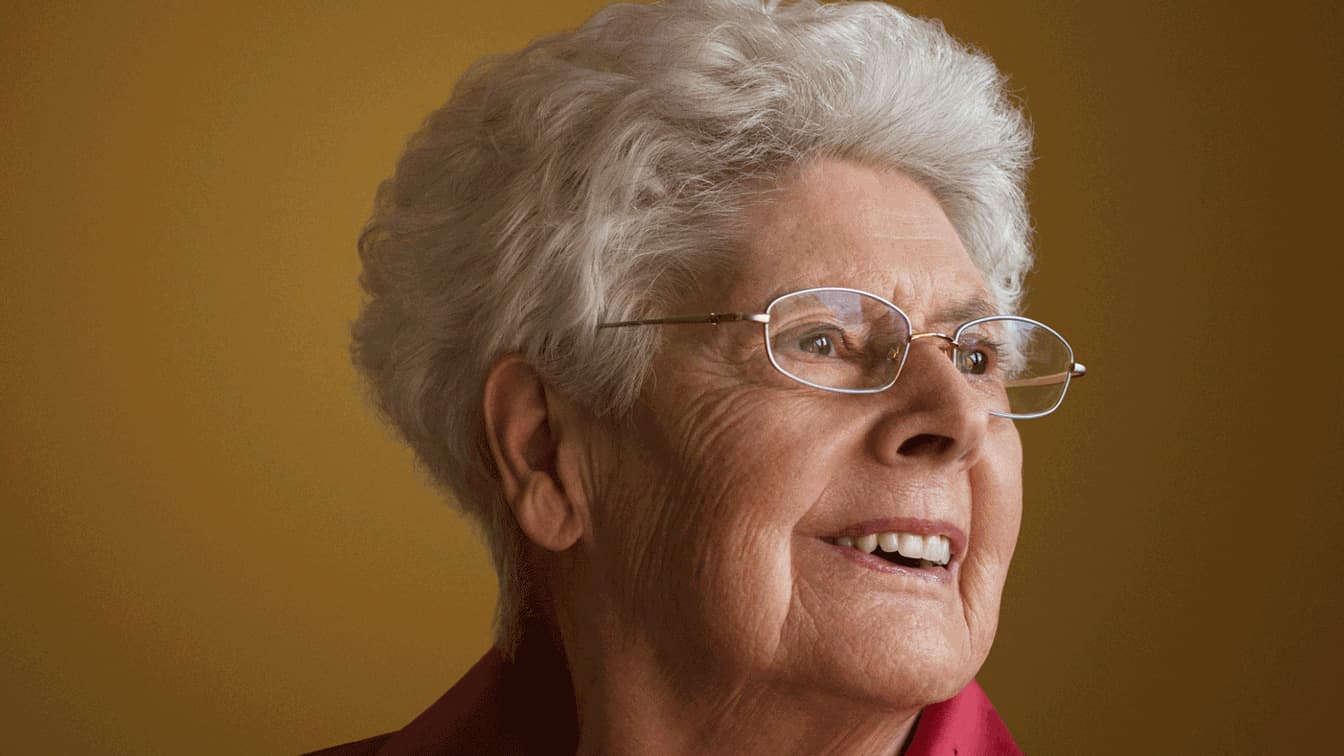 Portrait d'une vieille dame aux cheveux blancs et aux lunettes qui sourit.