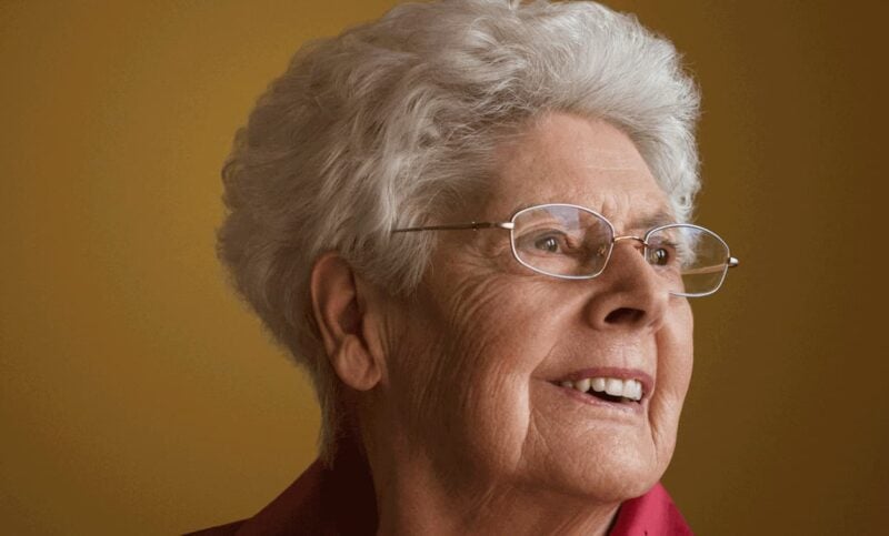 Portrait einer alten Dame mit weissen Harren und Brille, die lächelt.