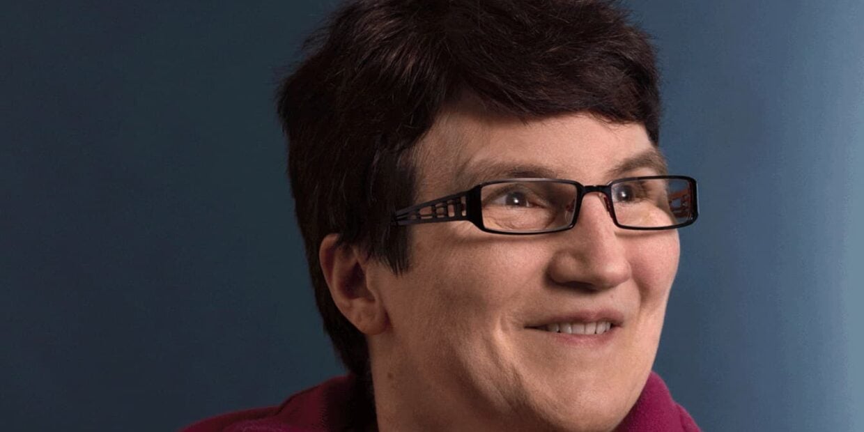 Portrait einer Dame mit braunen Harren und Brille die lächelt.