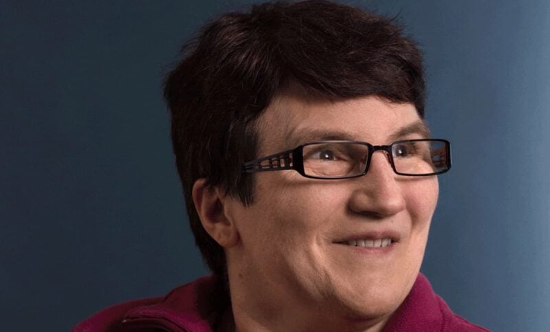 Portrait einer Dame mit braunen Harren und Brille die lächelt.