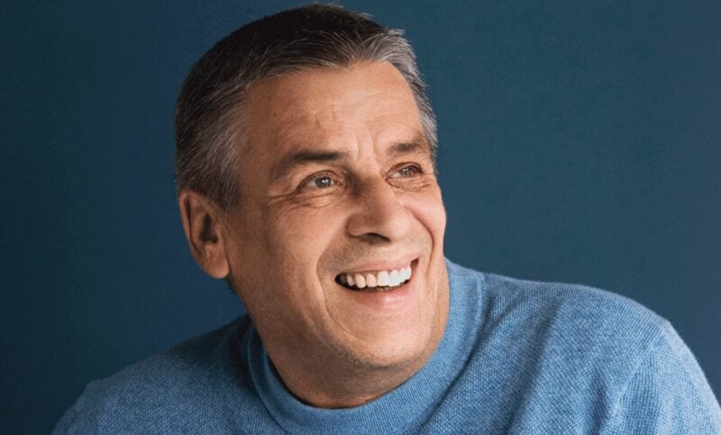 Portrait eines älteren Herrn der lächelt und einen blauen Pullover trägt.